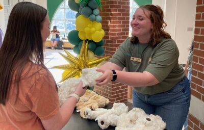 Campus Engagement Chair, Kylie Kelly, handing a student a teddy bear stuffing kit