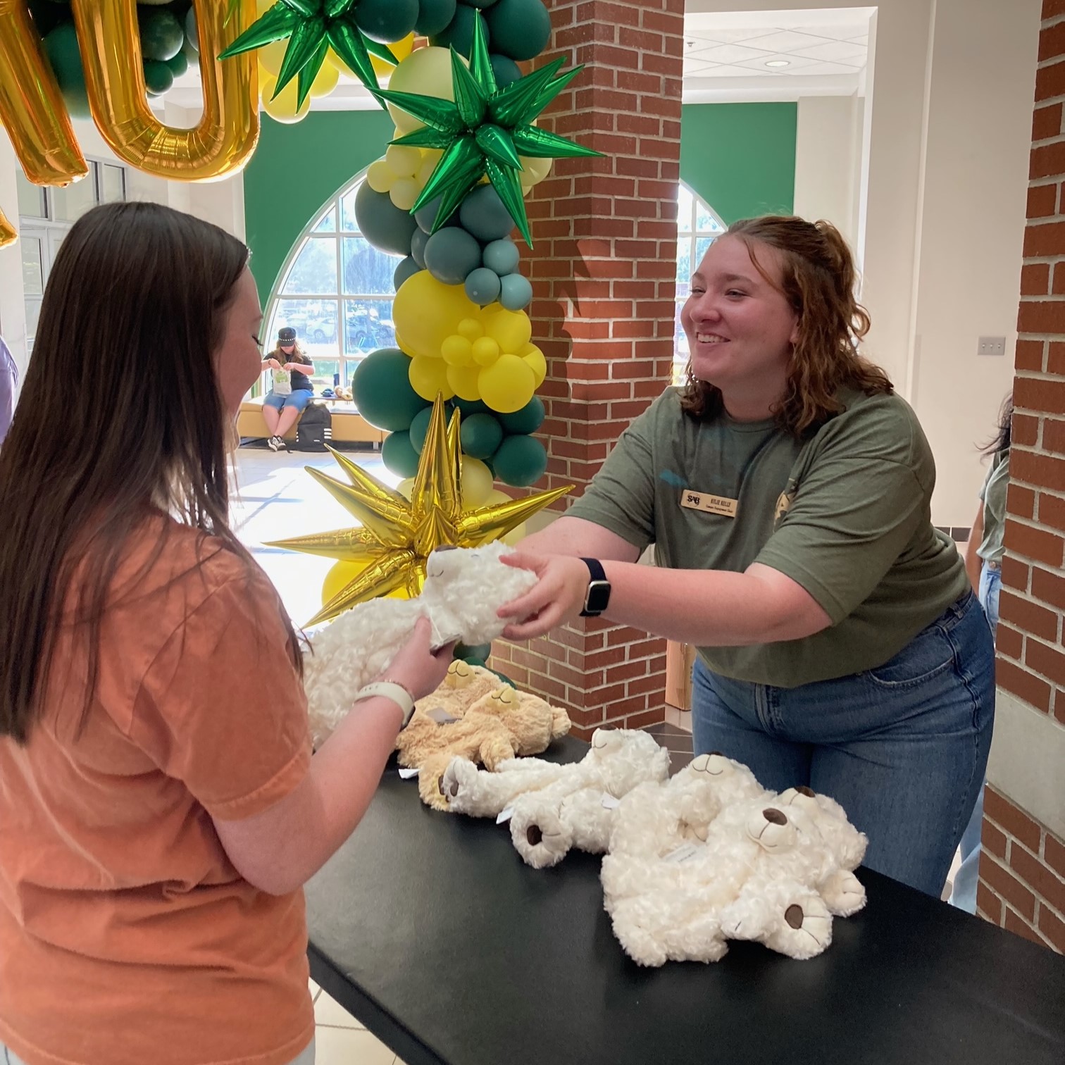 Campus Engagement Chair, Kylie Kelly, handing a student a teddy bear stuffing kit